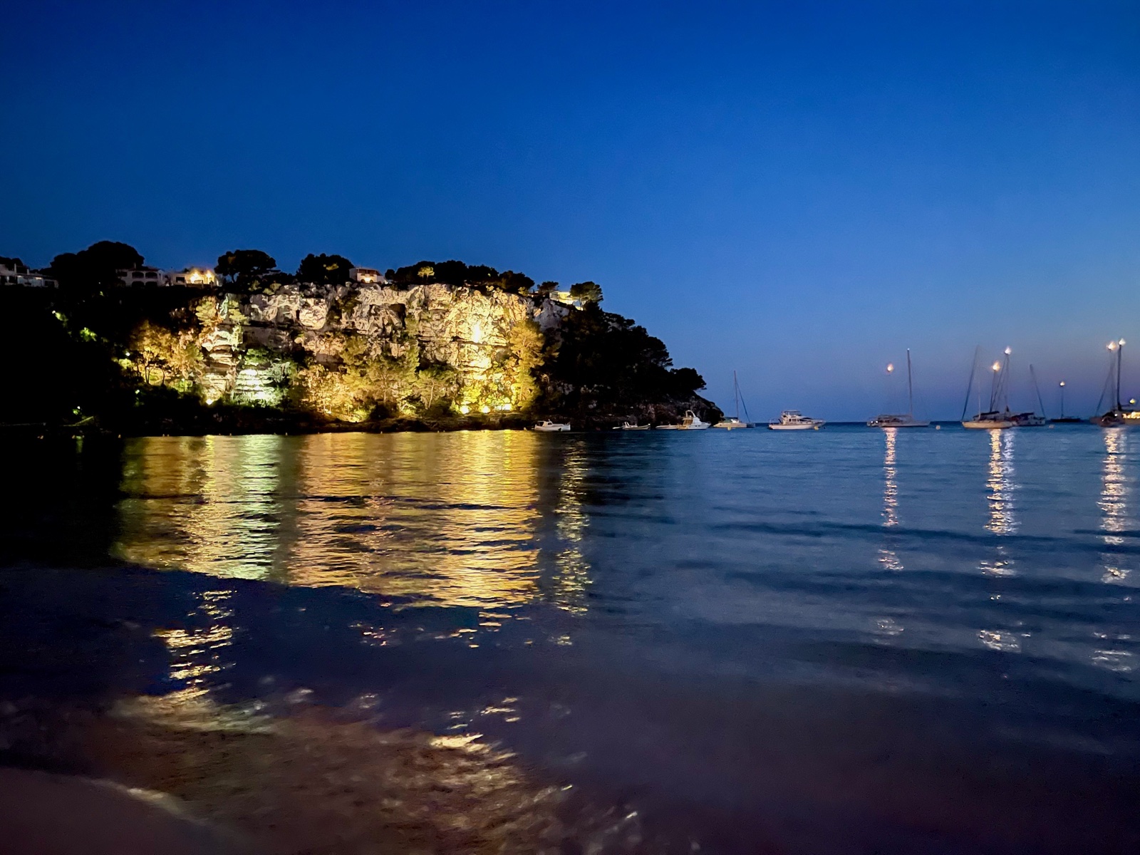 Badia de Cala Galdana de nit — penya-segats il·luminats reflectits en aigües calmes