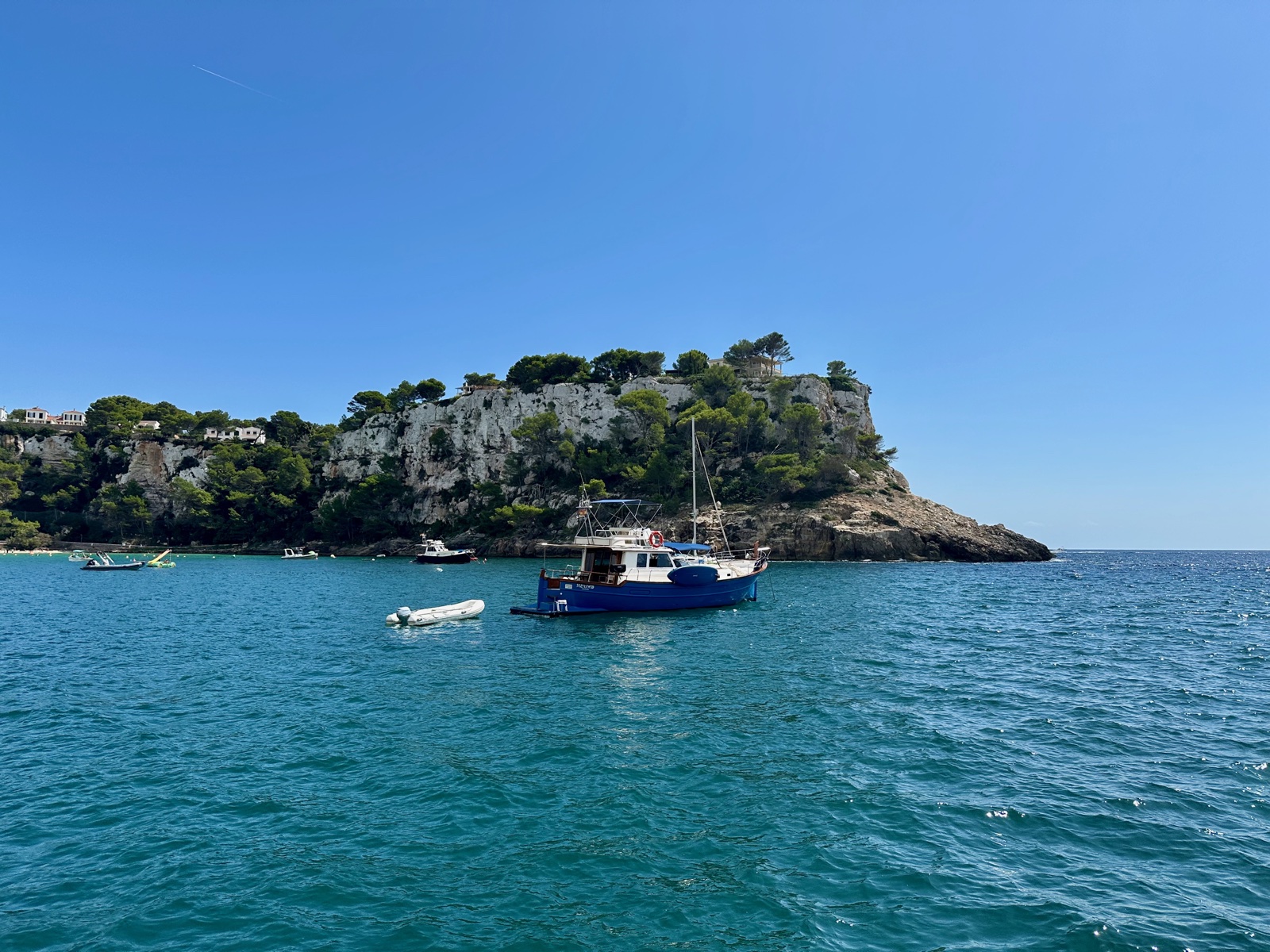Barca de pesca blava amarrada a les calmes aigües turqueses de la badia