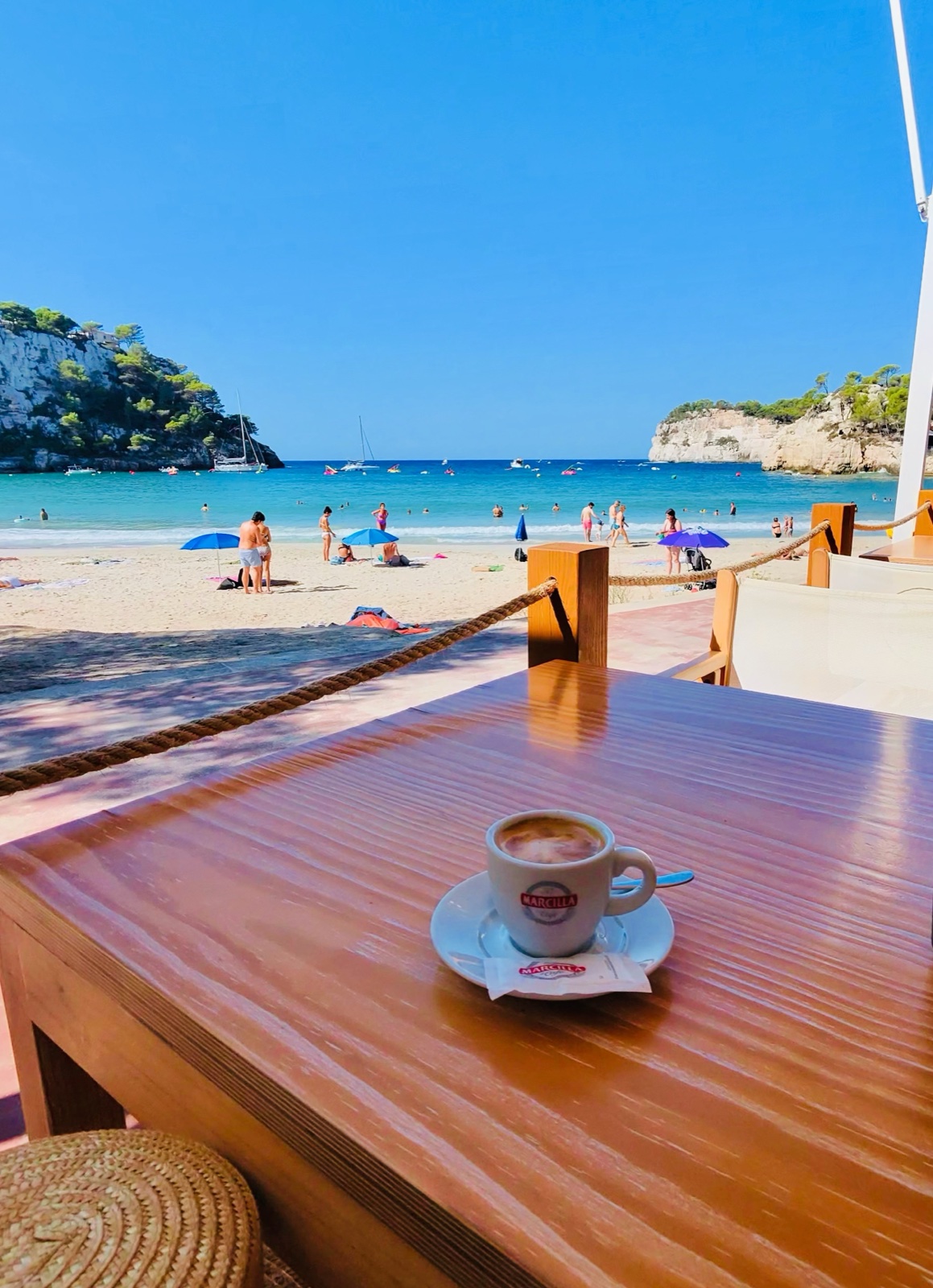 Cafè en una taula de terrassa de platja amb vistes a la platja de Cala Galdana